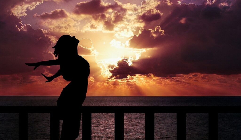 Mindful Breathing: 5 Science-Backed Techniques to Calm Your Mind and Body 3 Silhouette of a woman practicing mindful breathing on a balcony at sunset, with arms open and ocean in the background, evoking peace and freedom.